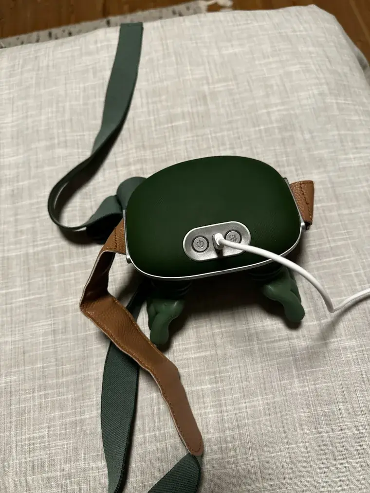 Il massaggiatore su un cuscino di lino, la fascia verde-marrone srotolata, cavo di ricarica collegato
